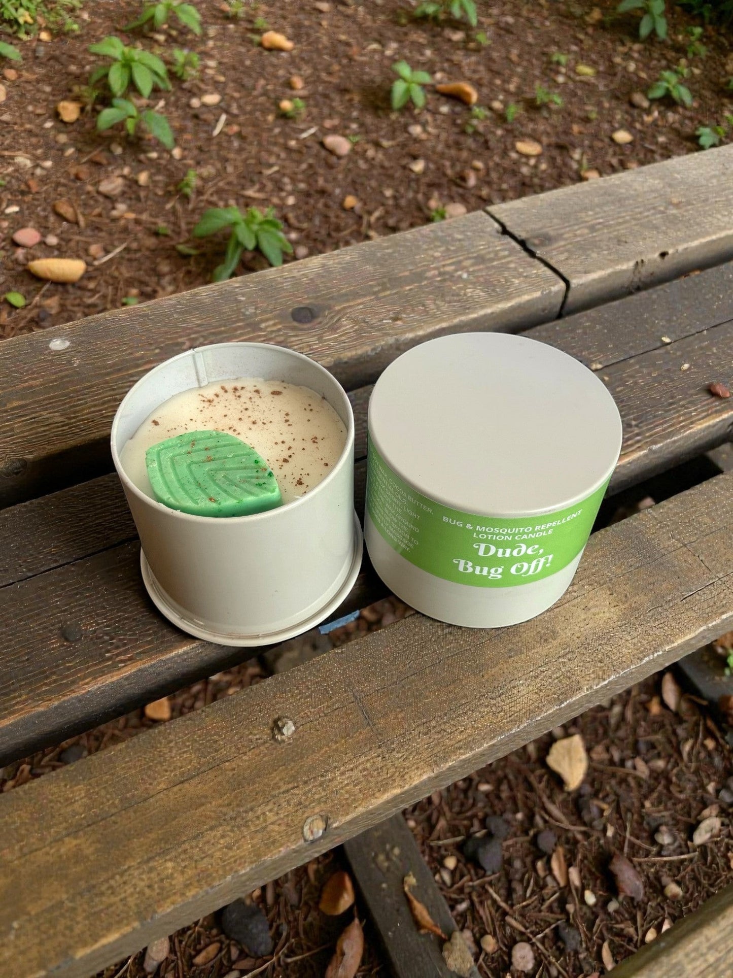 Harry’s Mama’s Faves: Lotions & Potions Dude, Bug Off! lotion candle in a tin with a green leaf accent on a bench.